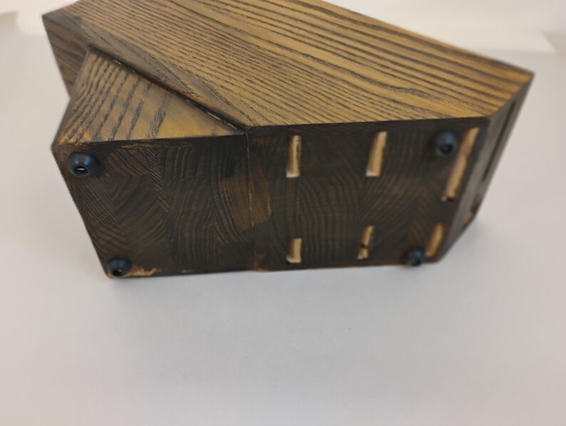 May include: A dark brown wooden knife block with a visible wood grain pattern. The base features four small black circular rubber feet attached to the bottom surface, providing stability and preventing the block from sliding on flat surfaces.