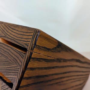 May include: A dark brown wooden knife block featuring a prominent wood grain pattern and multiple rectangular slots for storing kitchen knives. The block has a slanted top surface and a sturdy construction with visible joinery along the edges.