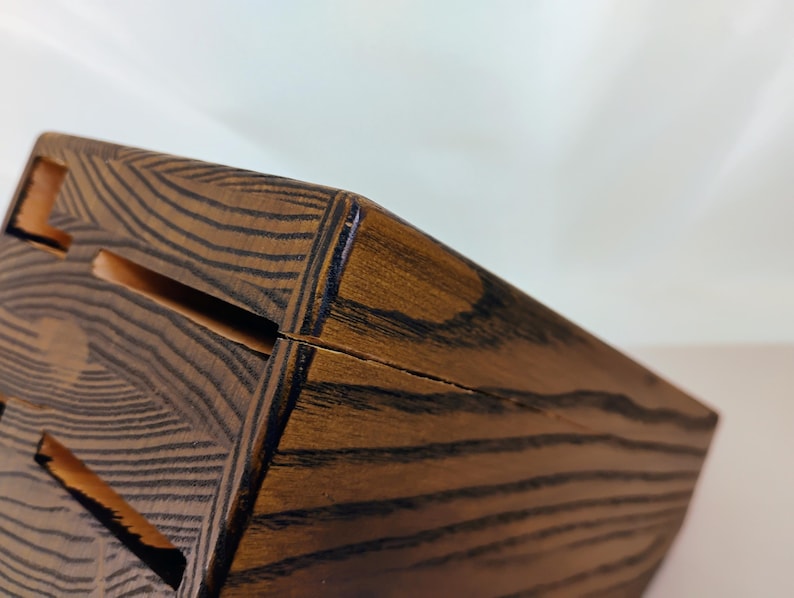 May include: A dark brown wooden knife block featuring a prominent wood grain pattern and multiple rectangular slots for storing kitchen knives. The block has a slanted top surface and a sturdy construction with visible joinery along the edges.