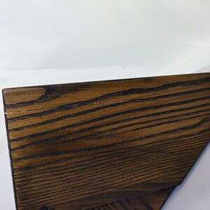 May include: A dark brown wooden shelf with a prominent, visible grain pattern. The shelf features a flat top surface and an angled side profile, showcasing the natural texture and deep, rich tones of the wood material in a simple, functional design.
