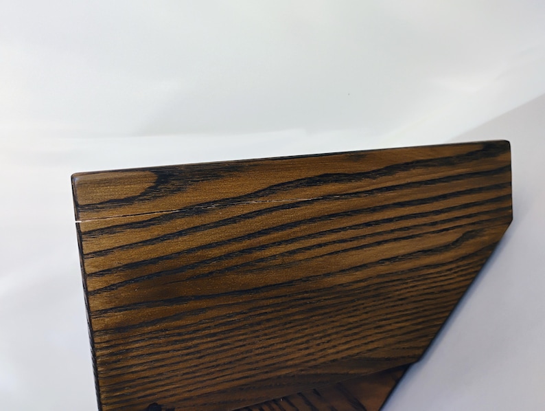 May include: A dark brown wooden shelf with a prominent, visible grain pattern. The shelf features a flat top surface and an angled side profile, showcasing the natural texture and deep, rich tones of the wood material in a simple, functional design.