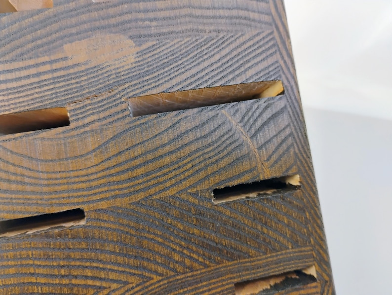 May include: A dark brown wooden knife block featuring a prominent natural wood grain pattern and multiple horizontal slots for storing kitchen knives. The block has a rectangular shape with a stained finish that highlights the wood texture.