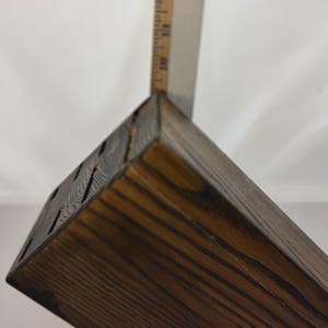 May include: A dark brown stained wooden knife block with visible wood grain and multiple rectangular slots on the top surface, positioned next to a metal ruler showing a measurement of approximately 8 inches in height for the block.