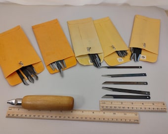 Könnte beinhalten: Ein Set aus Metall-Bastelklingen in fünf gelben Umschlägen, begleitet von einem Werkzeug mit Holzgriff und zwei Holzlinealen. Die Lineale zeigen Maße in Zoll und Zentimetern, wobei das längere Lineal eine Länge von 30 Zentimetern aufweist.