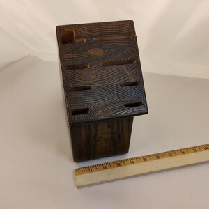 May include: A dark brown wooden knife block with a visible wood grain pattern and multiple slots for storage. A wooden ruler is positioned in front of the block, showing a length of approximately 11 inches for the ruler itself.
