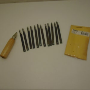 May include: A set of wood carving tools, including a wooden-handled chisel and multiple metal blades. A yellow package with the text "ONE DOZEN" is also present. The tools are arranged on a white surface.