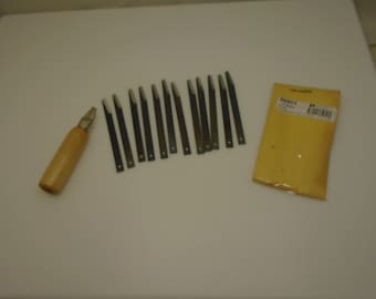 Könnte beinhalten: Ein Satz Holzbearbeitungswerkzeuge, darunter ein Meißel mit Holzgriff und mehrere Metallklingen. Eine gelbe Verpackung mit dem Text "ONE DOZEN" ist ebenfalls vorhanden. Die Werkzeuge sind auf einer weißen Oberfläche angeordnet.