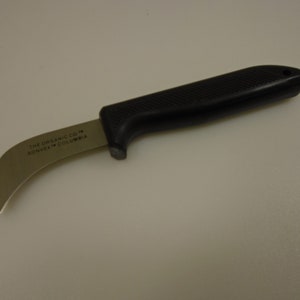 May include: A black handled curved knife with a silver blade. The blade is marked "THE ORGANIC CO. KONVEX COLUMBIA".