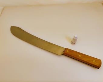 Könnte beinhalten: Eine große Machete mit gebogener Klinge, Holzgriff und Messingnieten. Die Klinge ist silberfarben und der Griff hellbraun. Neben der Machete steht eine kleine Flasche Mineralöl.