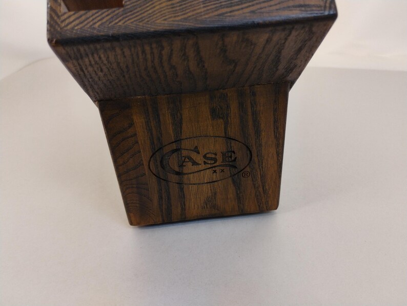 May include: A dark brown wooden knife block with a tapered, trapezoidal shape and a visible wood grain texture. The front face features the black printed text CASE XX inside an oval border, with a registered trademark symbol to the right.