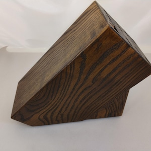 May include: A dark brown wooden knife block with a prominent wood grain pattern. The block features an angled top surface with multiple vertical slots for storing kitchen knives, constructed from solid wood with a deep, stained finish.