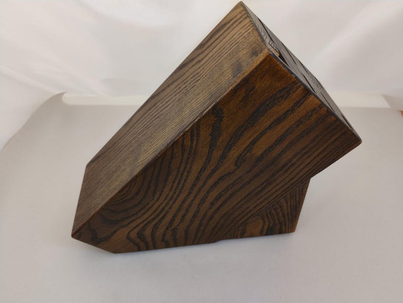 May include: A dark brown wooden knife block with a prominent wood grain pattern. The block features an angled top surface with multiple vertical slots for storing kitchen knives, constructed from solid wood with a deep, stained finish.
