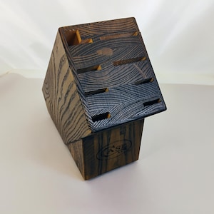 May include: A dark brown wooden knife block with a prominent wood grain pattern and an angled top featuring multiple slots for knife storage. The front of the base displays a circular logo with the text CASE in a bold, capitalized font.