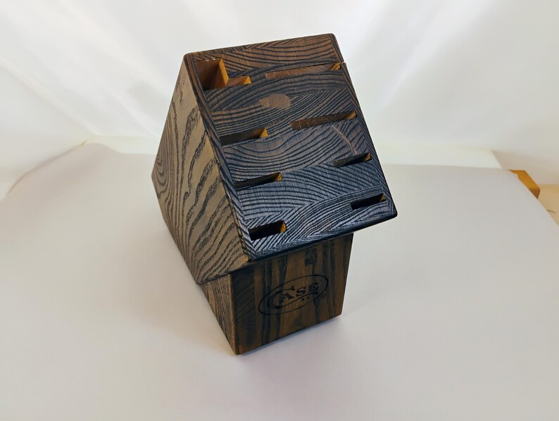 May include: A dark brown wooden knife block with a prominent wood grain pattern and an angled top featuring multiple slots for knife storage. The front of the base displays a circular logo with the text CASE in a bold, capitalized font.