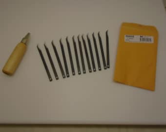 May include: A set of 15 small, curved, metal blades for leather crafting. The blades are arranged in a row on a white surface. A wooden handle for a leather crafting tool is also visible in the image. A brown envelope with the number 86808 printed on it is in the background.