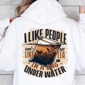 Peut inclure: Sweat-shirt blanc avec un motif graphique représentant un sachet de thé immergé dans l'eau. Le texte dit "J'aime les gens comme j'aime mon thé dans un sachet sous l'eau."