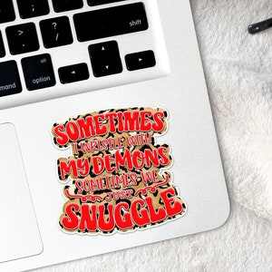 May include: A sticker with a leopard print background and red text that reads "Sometimes I wrestle with my demons sometimes we just snuggle."