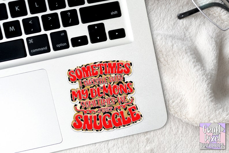 May include: A sticker with a leopard print background and red text that reads "Sometimes I wrestle with my demons sometimes we just snuggle."