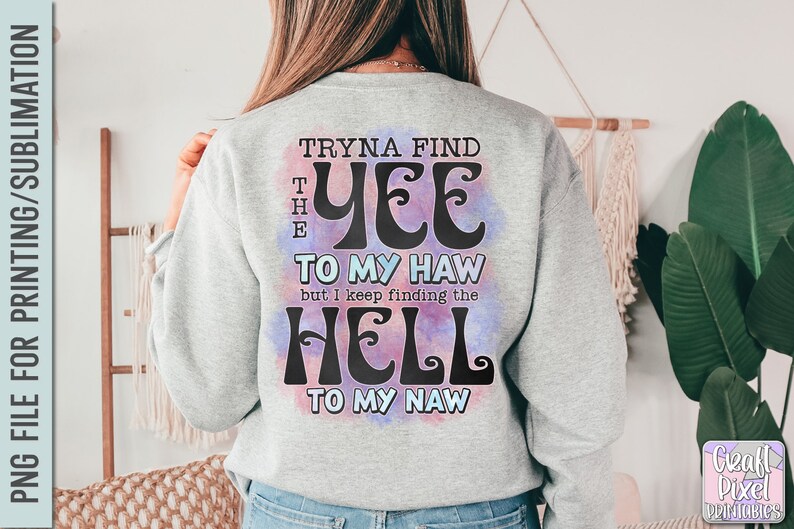 May include: A light gray sweatshirt with the text "Tryna Find The Yee To My Haw but I keep finding the Hell To My Naw" in a whimsical font. The text is over a watercolor-style background with purple and blue hues. The sweatshirt is a casual style.