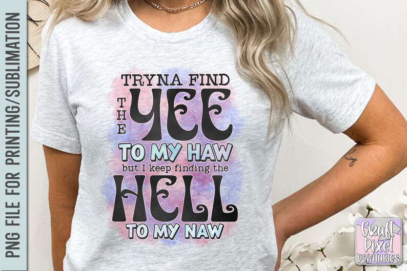 May include: Light gray t-shirt with the text "Tryna Find The Yee To My Haw but I Keep Finding The Hell To My Naw" in black, with a watercolor effect in pink and blue. The shirt is a casual wear item.
