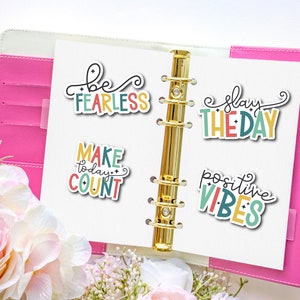 May include: A pink planner with gold rings and four colorful stickers with motivational quotes: "be fearless", "make today count", "slay the day", and "positive vibes".