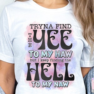 May include: White t-shirt with the text "Tryna Find The Yee To My Haw but I keep finding the Hell To My Naw" in a black, retro font. The text is set against a watercolor-style background with pink and blue hues.