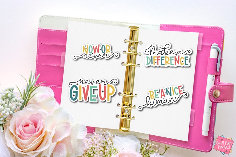 May include: Four colorful motivational stickers with positive messages: "Now or never", "Never give up", "Make a difference", and "Be a nice human". The stickers are placed on a pink binder with a gold ring mechanism.