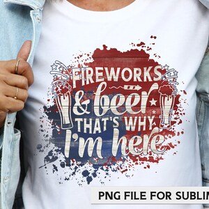 Puede incluir: Una camiseta blanca con un dise&ntilde;o gr&aacute;fico rojo, blanco y azul. El gr&aacute;fico presenta un fondo de tablones de madera con el texto "Fireworks & beer that's why I'm here" y dos vasos de cerveza. El gr&aacute;fico est&aacute; rodeado de salpicaduras de pintura roja, blanca y azul.
