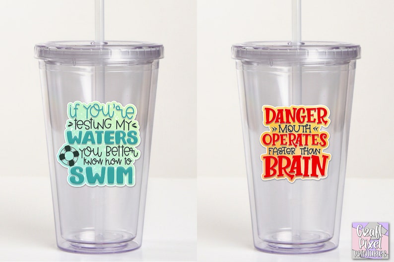 May include: Two clear plastic tumblers with reusable straws. The tumbler on the left has a teal and blue graphic that says "If you're testing my waters you better know how to swim". The tumbler on the right has a red graphic that says "Danger >>Mouth Operates Faster Than Brain".