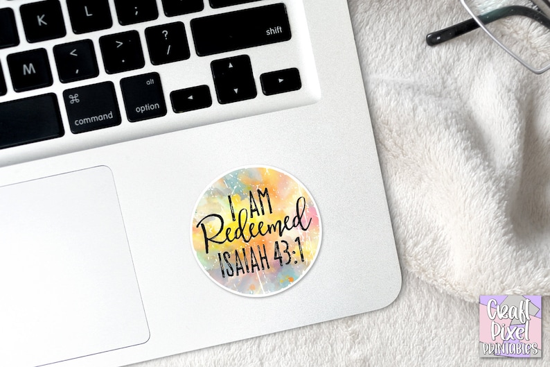 May include: A round sticker with a watercolor background in shades of yellow, orange, pink, and blue. The sticker features the text "I AM Redeemed ISAIAH 43:1" in black.