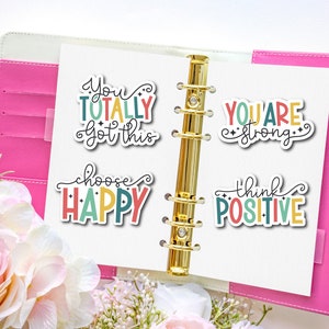 May include: Four colorful motivational stickers with positive messages: "You totally got this", "Choose Happy", "You are strong", and "Think Positive". The stickers are on a white page in a pink binder.