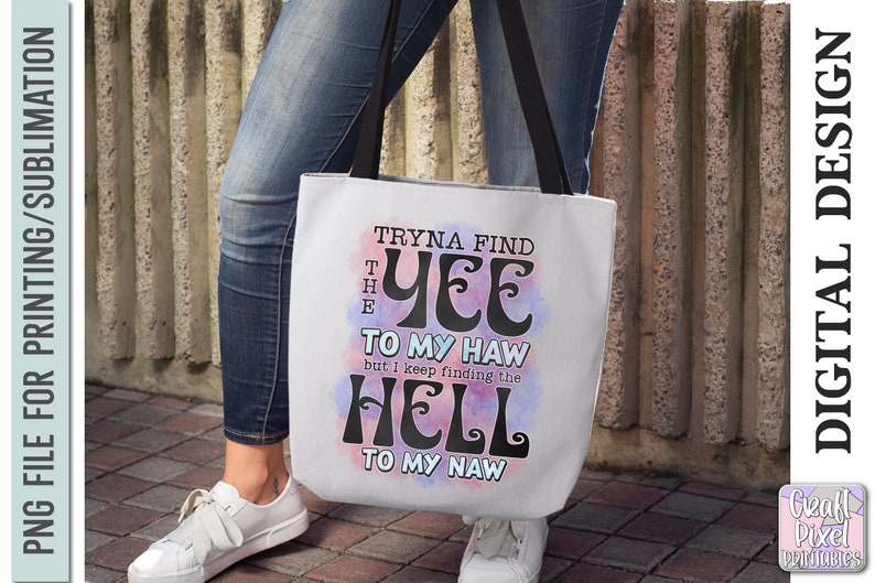 May include: White tote bag with black handles featuring the text "Tryna find the Yee to my Haw but I keep finding the Hell to my Naw" in a whimsical font. The design includes pink and blue watercolor-style accents.