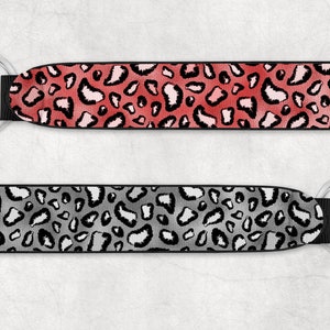 May include: Two keychains with a leopard print design. The top keychain is red and pink, while the bottom keychain is gray and white.