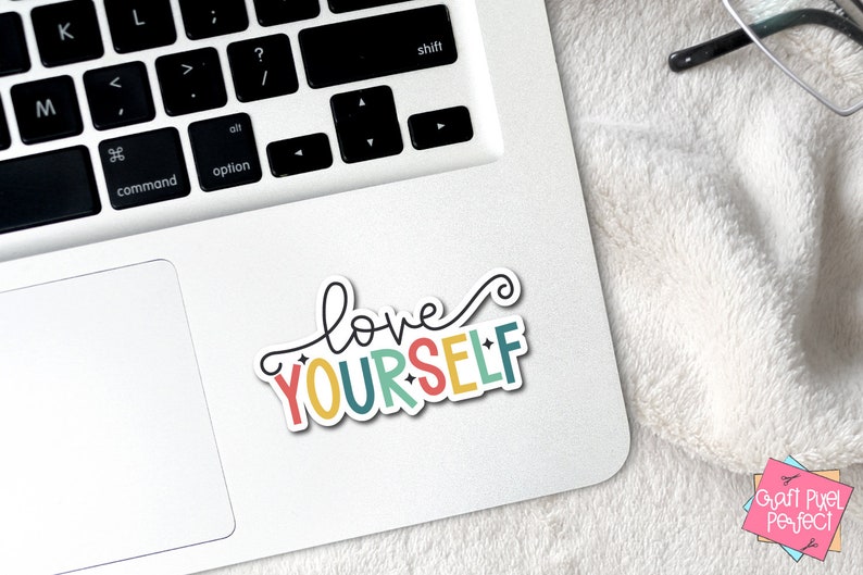 May include: A colorful sticker with the text "love yourself" in a white outline. The sticker is on a white laptop.