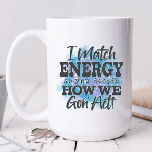 May include: White ceramic mug with a blue and purple watercolor design. The mug has black text that reads "I Match Energy so you decide How We Gon' Act!"