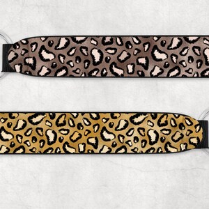 May include: Two keychains with black fabric and silver key rings. The fabric has a leopard print pattern. One keychain has a brown and beige leopard print, and the other has a gold and beige leopard print.