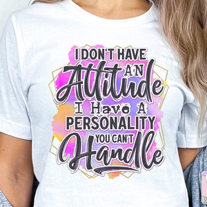 Puede incluir: Camiseta blanca con el texto "I don't have an attitude, I have a personality you can't handle" en escritura negra. El texto est&aacute; sobre un fondo de acuarela colorido con un marco geom&eacute;trico dorado.