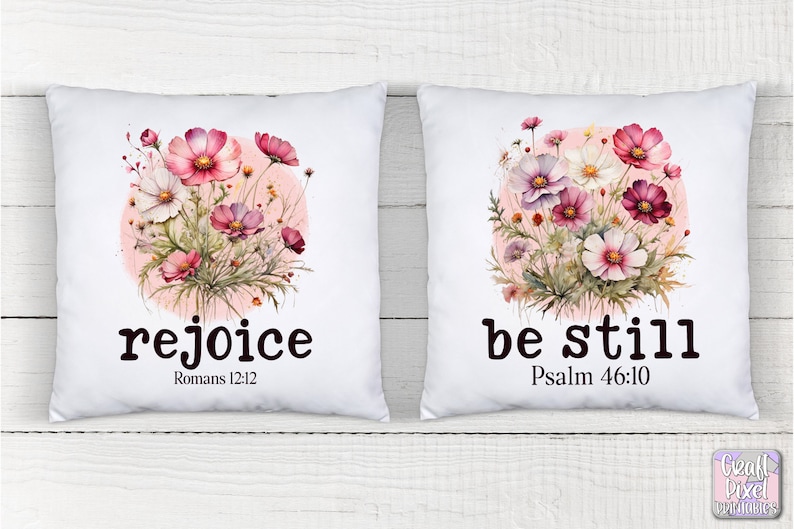 May include: Two white pillow covers with floral designs and inspirational quotes. The left pillow features pink and white flowers with the quote "rejoice" and the scripture reference "Romans 12:12". The right pillow features the same floral design with the quote "be still" and the scripture reference "Psalm 46:10".