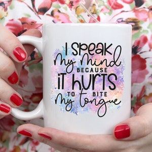 K&ouml;nnte beinhalten: Eine wei&szlig;e Keramiktasse mit einem bunten Aquarellhintergrund und dem Text "Ich sage meine Meinung, weil es weh tut, sich auf die Zunge zu bei&szlig;en".