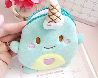 May include: A light blue plush toy shaped like a narwhal with a pink heart on its chest. The narwhal has a white and brown ice cream cone on its head. The toy is sitting on a calendar with the text "@lulusweetkawaiishop" printed on it.