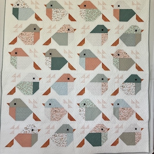 May include: A rectangular quilt featuring a repeating pattern of twenty stylized birds arranged in five rows and four columns. Each bird is constructed from various fabric patches in muted tones of sage green, dusty rose, and cream with floral prints.