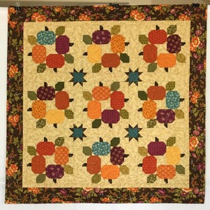 May include: A beige quilt with a brown floral border. The quilt features a repeating pattern of orange, red, green, and blue geometric shapes.