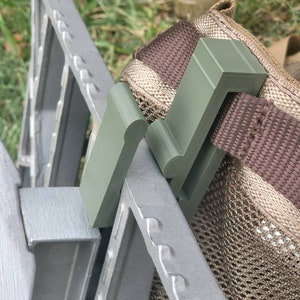 May include: A green plastic clip attached to a brown and tan mesh bag. The clip is designed to attach to a metal frame.