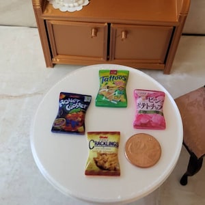 May include: Four miniature bags of chips on a white surface. The bags are green, blue, pink, and orange. The bags have different brand names and logos. The bags are all about 2 inches tall.