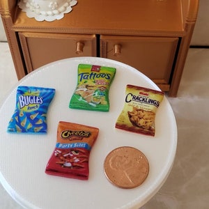 May include: Four miniature bags of chips on a white surface. The bags are for Bugles Ranch, Cheetos Party Size, Tater Tots corn chips, and Cracklings Salt & Vinegar.