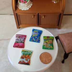 May include: A white table with four miniature bags of chips. The bags are labeled "Bugles", "Tattoos", "Clover Chips", and "Potato Chips". There is a penny on the table.
