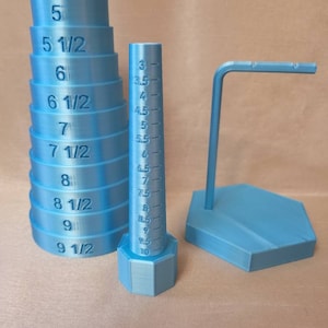 May include: A blue plastic ring sizer with a graduated cone and a stack of rings. The rings are marked with sizes from 5 to 9 1/2. The sizer also includes a stand with a hexagonal base.