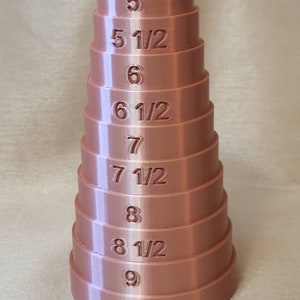 May include: A stack of 10 ring sizers made of a light brown plastic. The sizers are numbered from 5 to 9 1/2.