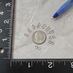 May include: A close-up of a silver US dime coin surrounded by a circle of small silver jump rings. The jump rings are about the size of the coin.