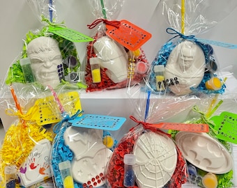 May include: Ten clear plastic bags filled with colorful tissue paper and craft supplies. Each bag contains a white ceramic figure of a superhero, such as Spiderman, Batman, and Hulk. The bags are tied with a ribbon and a small tag that says "Thank you for coming to Isla's party!"